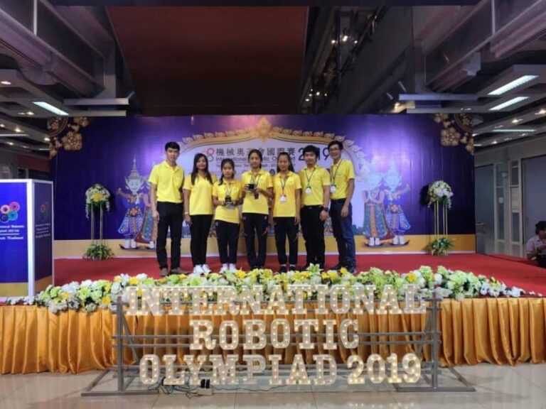 นักเรียนและครูเสื้อเหลืองถ่ายรูปบนเวที International Robotic Olympiad 2019