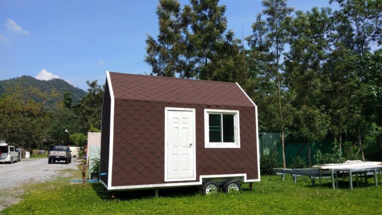 บ้านน็อคดาวน์หรือบ้านเคลื่อนที่หลังเล็กผนังสีน้ำตาลตั้งอยู่กลางสนามหญ้า